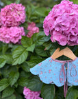Pink hydrangeas with a blue dress collar on a hanger against a green leafy background