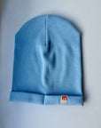Blue single rib cotton hat with a visible brand logo on a light gray background