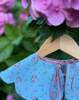 Blue floral dress  collar with pink trim on a wooden hanger against a pink flower background